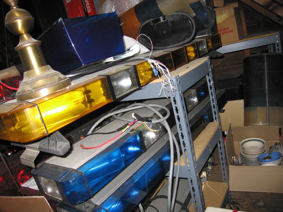 Several emergency light bars, some yellow and some blue, are stacked on shelves in what looks like storage