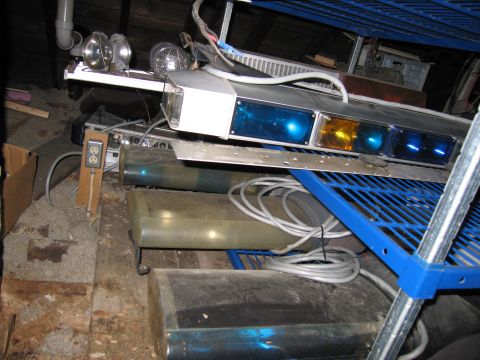 2001 Ford Crown Victoria - A collection of emergency vehicle lights and storage tanks are piled up in a dimly lit, cluttered space.