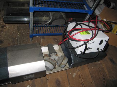 2001 Ford Crown Victoria - A white battery charger with red and black cables sits on a shelf next to other equipment, including a metal object with a mesh top.