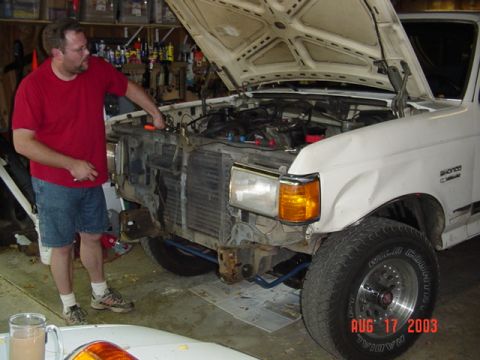1987 Ford Bronco - White Ford Bronco in a garage with its hood up and the grille, front bumper and driver-side headlight assembly removed, exposing the core s…