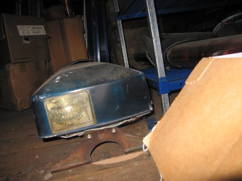 2001 Ford Crown Victoria - A detached blue headlight assembly rests on a wooden floor, surrounded by boxes and shelving.