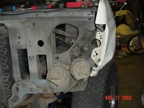 1987 Ford Bronco - Close-up inside the front of a truck with the fender removed, showing the bare inner apron and radiator support with two round horns mounte…