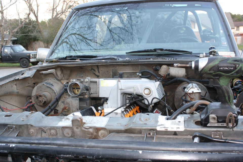 Engine bay with silver intake manifold, orange injector boots and a cordless impact driver on the rail