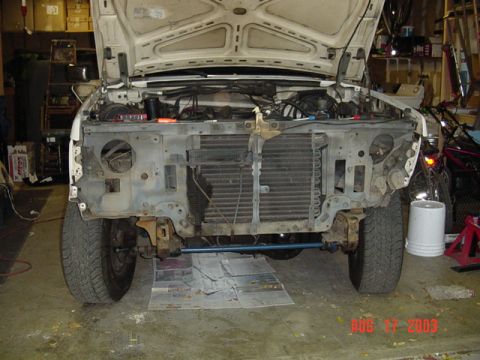 1987 Ford Bronco - Front end of a white Ford truck stripped down in a garage: grille, bumper, headlights and fenders removed to expose the radiator, core supp…