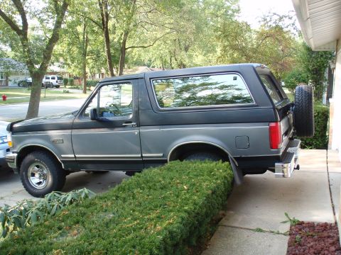 1993 Ford Bronco - This Ford Bronco is parked on a driveway next to a house and some bushes.