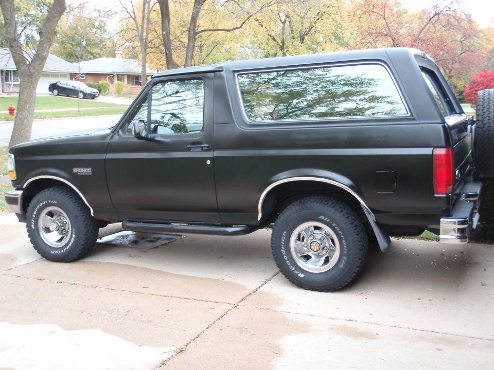 Black Ford Bronco SUV parked on driveway, side view. Chrome trim, BFGoodrich tires, spare tire on rear