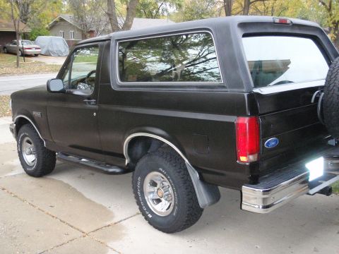 1993 Ford Bronco - This black Ford Bronco is parked on a concrete driveway with houses and trees in the background.