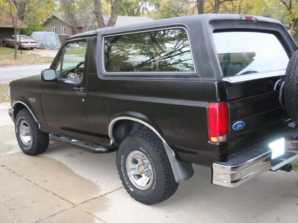 Black Ford Bronco parked on a driveway. Side view shows the front and rear tires, running boards, and spare tire on the back
