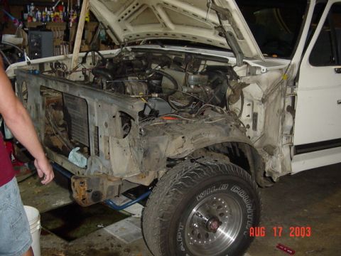 1987 Ford Bronco - White full-size Ford truck/SUV in a garage with the front clip stripped, both front fenders, grille and inner panels removed to expose the…
