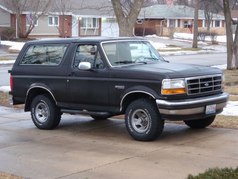 1993 Ford Bronco - This black Ford Bronco is parked in a suburban driveway during a cloudy day.