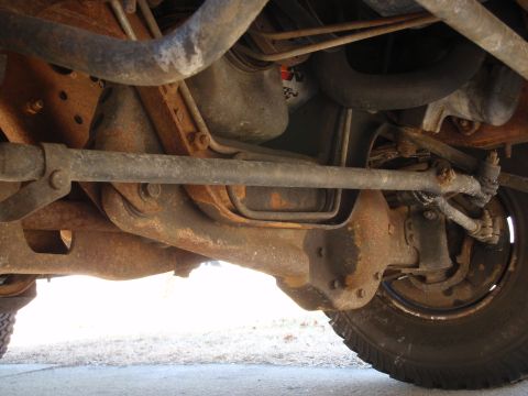 1993 Ford Bronco - The underside of a vehicle reveals rusty suspension parts and a tire.