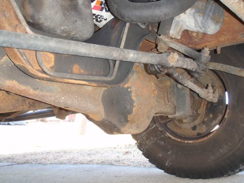 1993 Ford Bronco - This photo shows the rusty undercarriage of a vehicle, focusing on the front axle and steering assembly.
