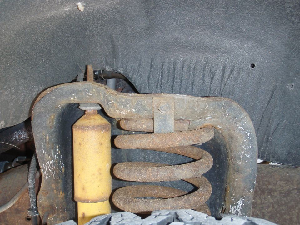 Rusty front suspension coil spring and yellow shock absorber, viewed from below