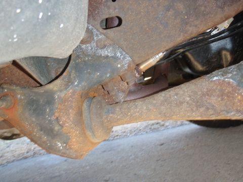 1993 Ford Bronco - Close-up view of an exhaust system component, likely an oxygen sensor, attached to rusted undercarriage parts.