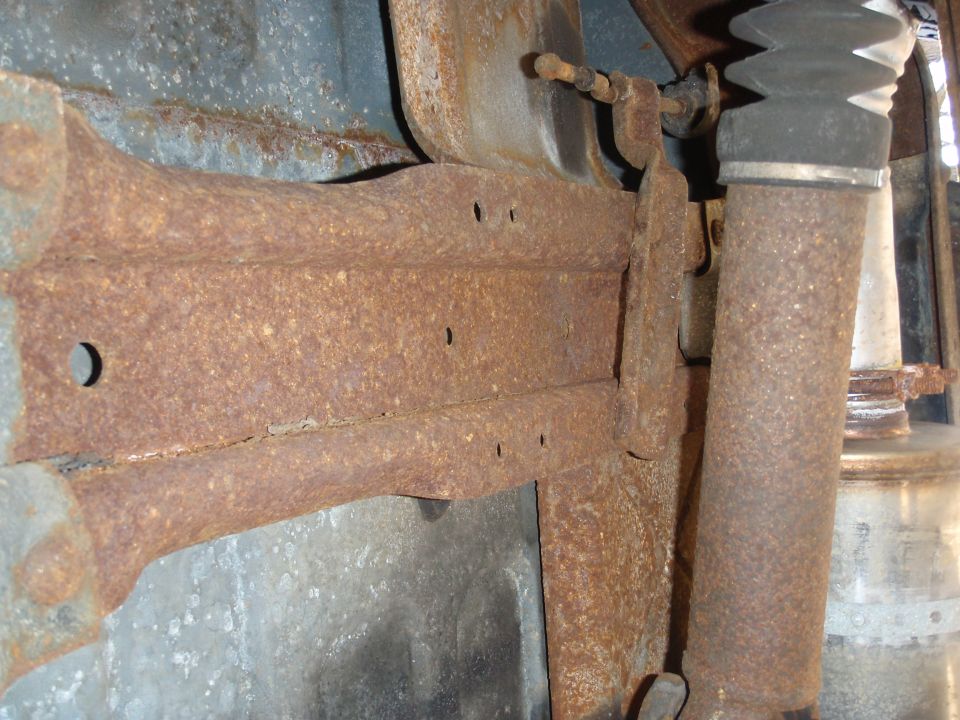Heavily rusted frame rail and suspension parts, including a shock absorber and exhaust pipe