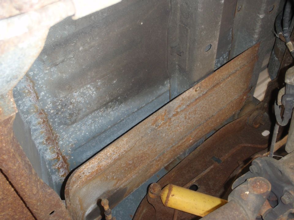 Close-up of rusty metal frame and yellow shock absorber under a vehicle