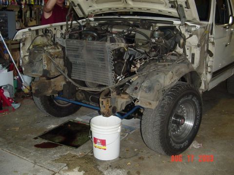 1987 Ford Bronco - Front three-quarter view of a white truck stripped for body work in a garage, both front fenders, grille, bumper and headlights removed to…
