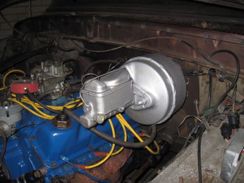 1979 Ford Bronco - Close-up of the brake booster and master cylinder assembly in an engine bay, a blue engine block and yellow spark plug wires.