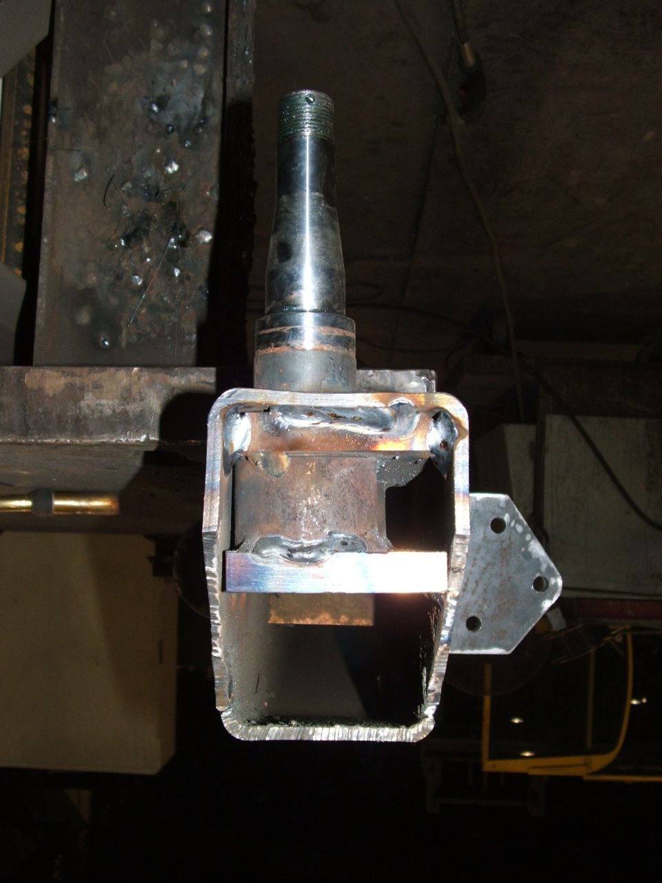 Welded metal bracket holding a metal spindle, with visible weld marks and rough edges