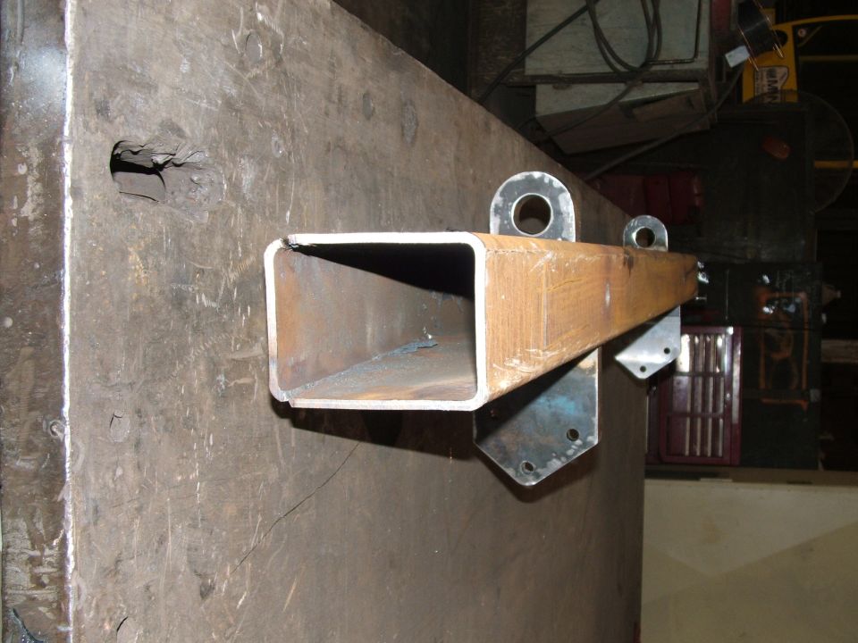 Fabricated metal bracket with a rectangular tube and two eyelets, mounted on a large metal surface