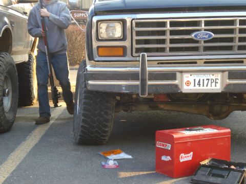 1985 Ford Bronco - A black Ford truck's front end is visible, with a red toolbox and another vehicle to the left.