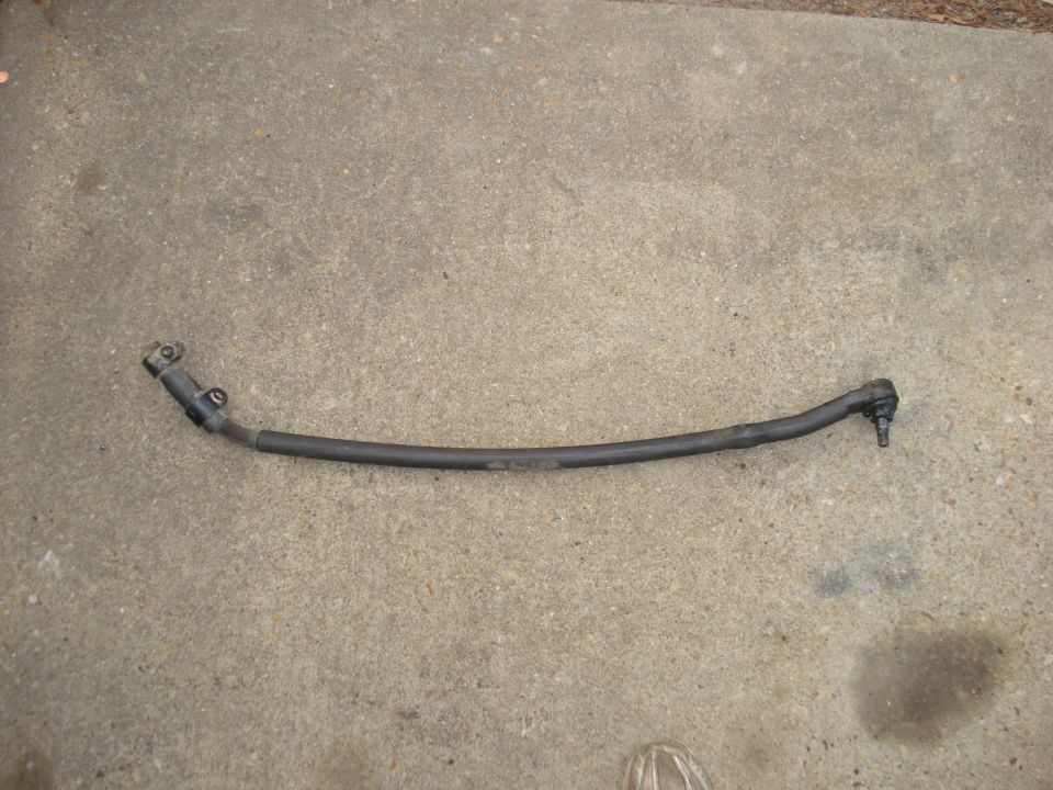 Steering linkage rod with ball joint ends, lying on concrete