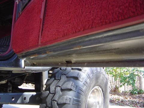 1986 Ford Bronco - The underside of a vehicle is visible, including a large tire and the lower part of the door.