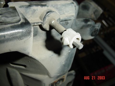 1987 Ford Bronco - Close-up of a dusty white-painted bench vise on a workbench, its threaded screw partly extended and a small metal bar clamped in the plasti…