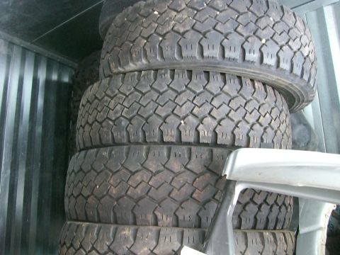 2005 Dodge 3500 - A vertical stack of used tires with aggressive all-terrain/mud tread, some still mounted on wheels, stored inside a corrugated metal shippi…