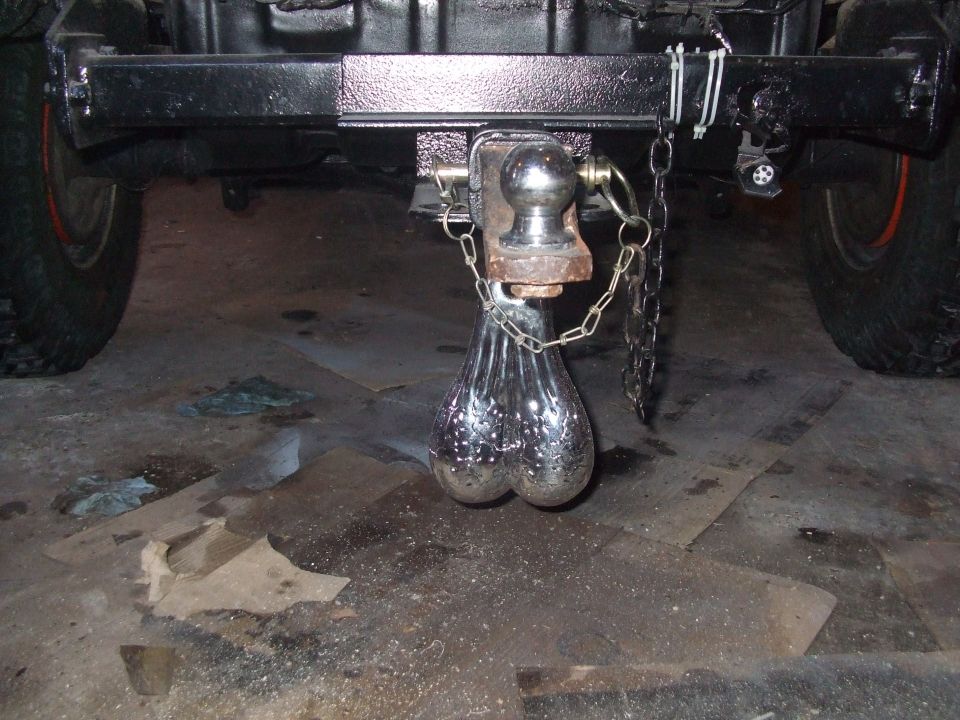 Hitch on a vehicle with chrome truck nuts hanging from it. Supermotors.net logo visible