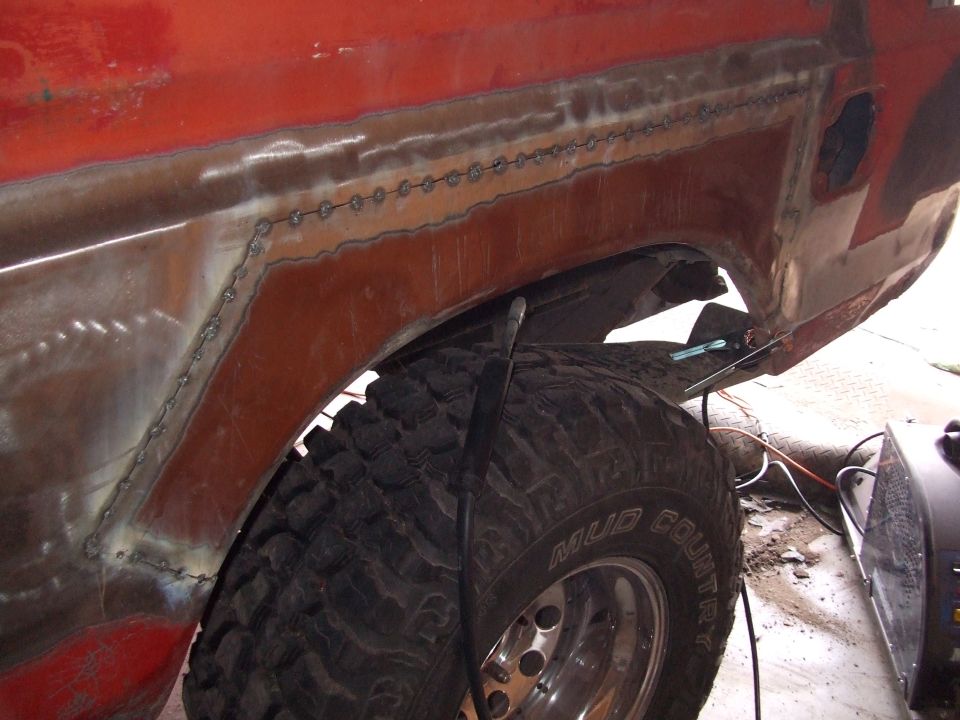 Close-up of red vehicle's rear fender area with fresh welds and a large off-road tire
