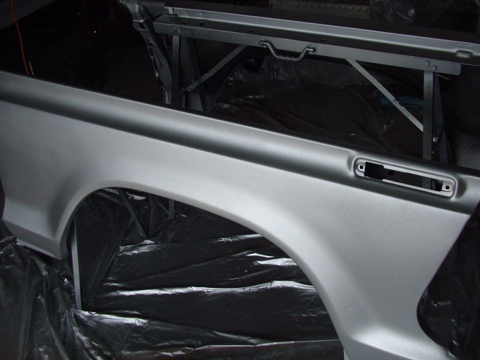 Silver painted rear fender and bed side panel on a stand, covered in plastic sheeting