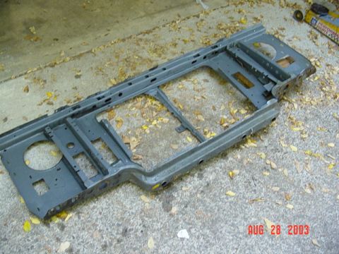 1987 Ford Bronco - A truck's stamped-steel radiator core support removed from the vehicle and laid on a leaf-strewn concrete driveway, coated in gray primer a…