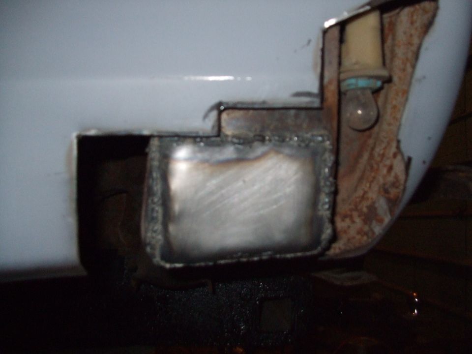 Close-up of a welded metal patch on a vehicle's rear corner, with a light bulb socket visible