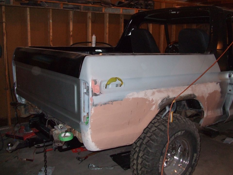 Rear quarter panel of a black and gray 1978 Ford Bronco undergoing bodywork, with primer and bondo visible
