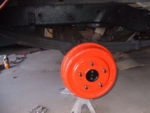 1979 Ford Bronco - A freshly painted orange brake drum is shown on jack stands with the vehicle's leaf springs visible above.