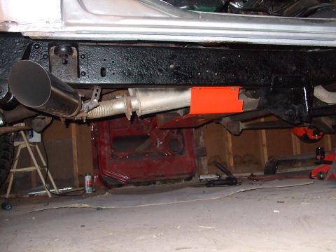 1979 Ford Bronco - The undercarriage of a vehicle is shown, a prominent exhaust system and an orange skid plate, with a red vehicle body visible in the backgr…