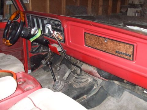 1979 Ford Bronco - The interior of a red vehicle shows a wood-grain trim panel with a "CUSTOM" badge and two gear shifters.