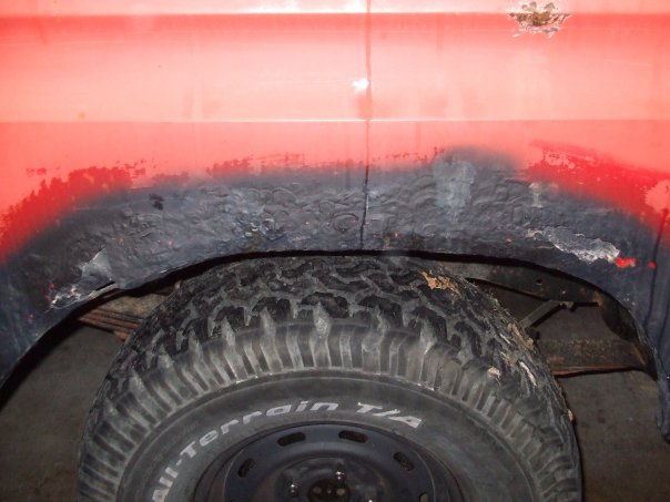 Close-up of a red vehicle's rear wheel well showing rust and a tire with 'All-Terrain T/A' visible