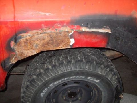1979 Ford Bronco - The rear wheel well of a red vehicle shows significant rust damage and repair work.
