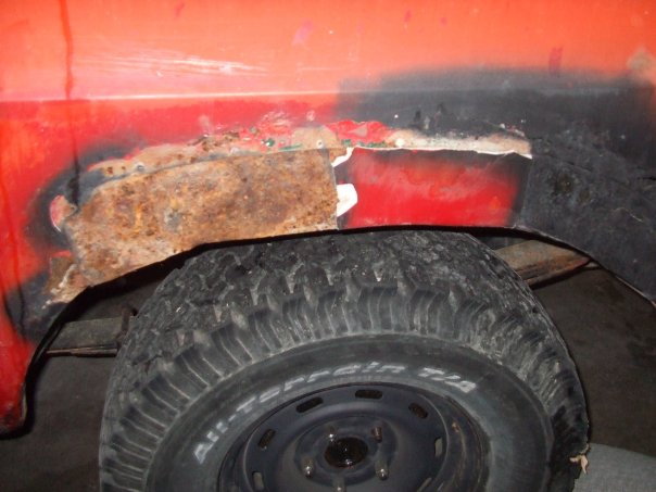 Red vehicle's rusted rear wheel well and tire