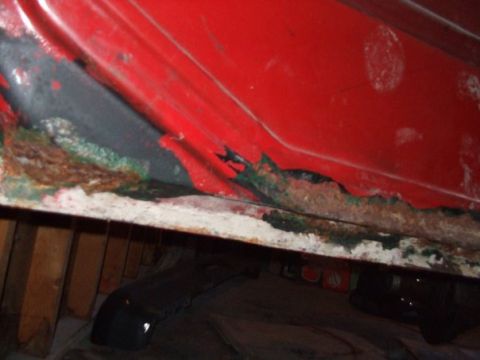 1979 Ford Bronco - The lower edge of a red car door shows extensive rust damage.