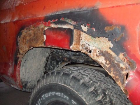1979 Ford Bronco - The rear wheel well of a red vehicle shows significant rust damage and deterioration.