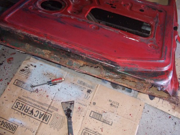 rusted red car door with tools on cardboard
