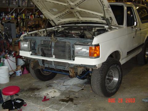 1987 Ford Bronco - White Ford Bronco in a home garage with the hood raised and the grille and front bumper removed, exposing the radiator, core support and bl…