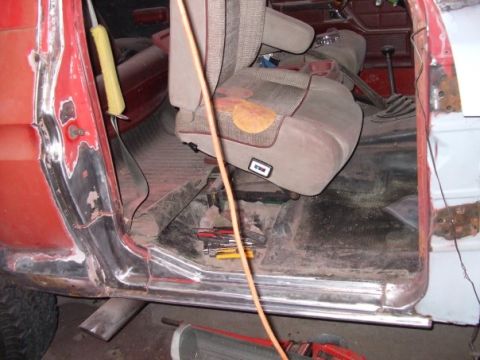 1979 Ford Bronco - The interior of a vehicle is visible, with tools on the floor and rust on the door frame.