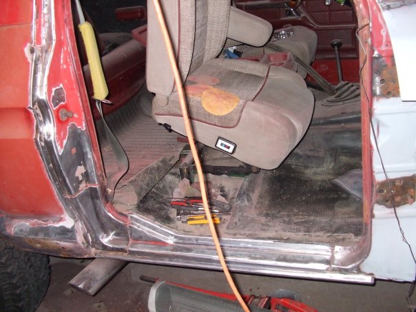 Interior of a vehicle undergoing bodywork, showing the driver's seat, door panel, and floor