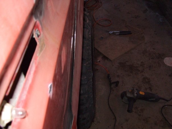 Red vehicle door with visible damage and a black tire next to it. An angle grinder and wires are on the floor