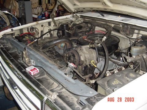 1987 Ford Bronco - Engine bay of a white Ford truck with the hood up and the driver-side fender removed, showing the V8 with black air cleaner, A/C compressor…