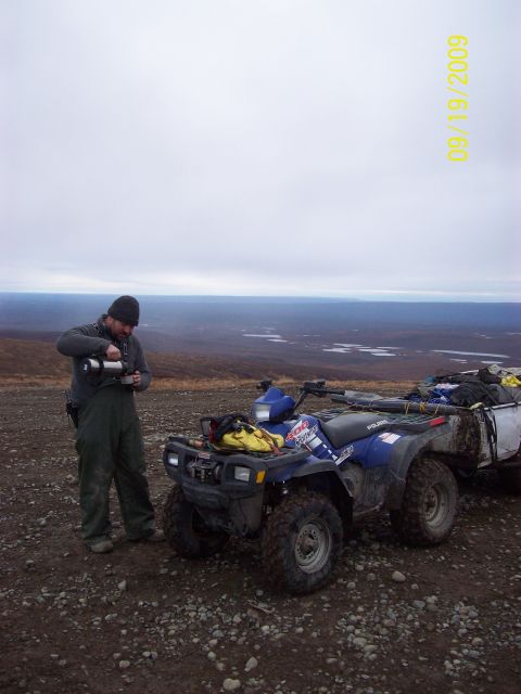 1986 Chevrolet Blazer - A man prepares a drink next to a blue ATV and trailer on a rocky terrain with a scenic overlook.